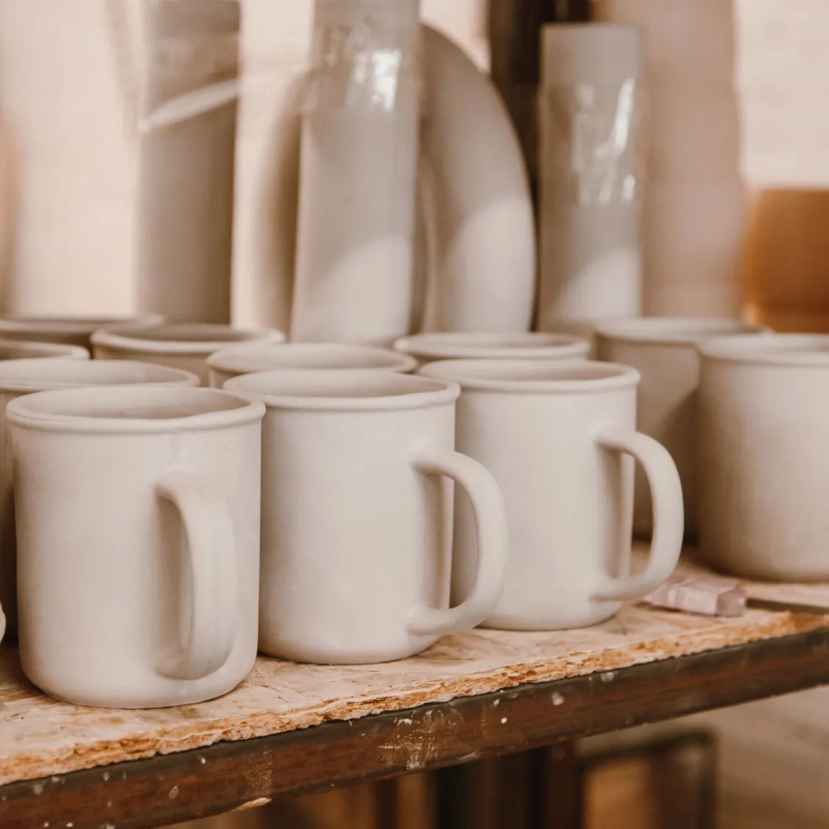 Unpainted white ceramic mugs lined up on a workshop shelf.
